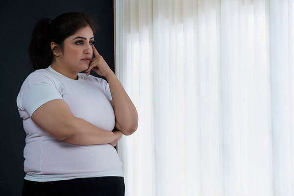 Sad obese woman looks while standing by the window