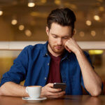Sad man with coffee and smartphone at restaurant