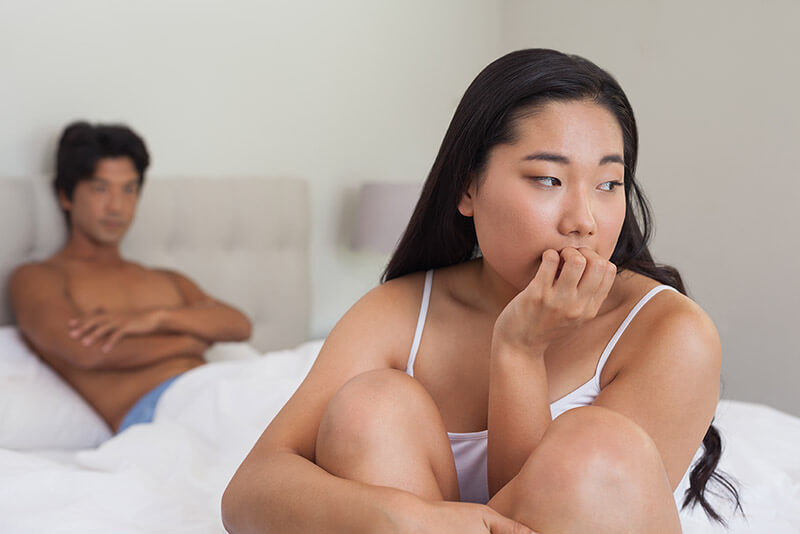 Boyfriend looking at upset girlfriend sitting on end of bed