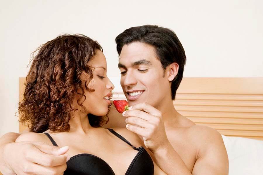 Close-up of a young man feeding a strawberry to a girl