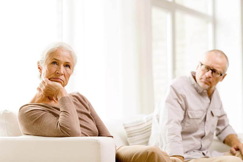 unhappy senior couple sitting on sofa at home