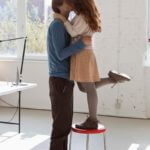 A young woman on a stool kissing her tall boyfriend