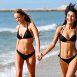 2 young women walking on beach while holding hands
