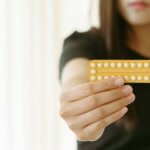Woman holding contraception pills at home, closeup