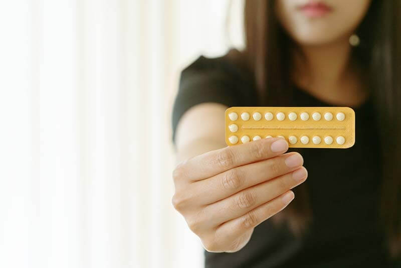 Woman holding contraception pills at home, closeup