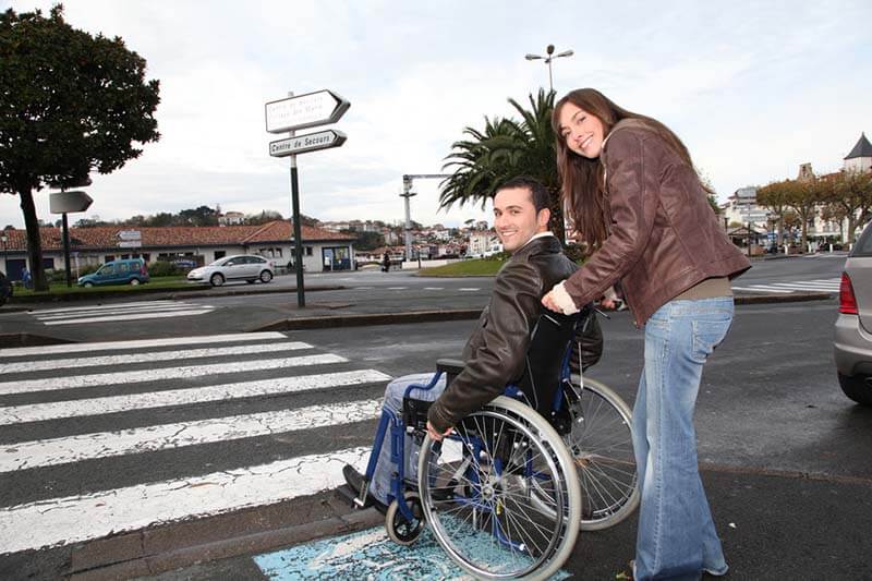 woman helpin gman in wheelchair cross a street