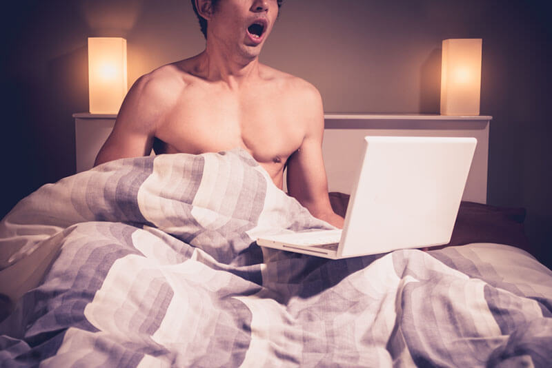 Young man masturbating to adult content on his laptop in bed