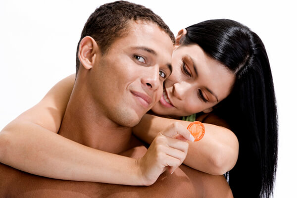 Young woman holding a condom embracing a young man from behind
